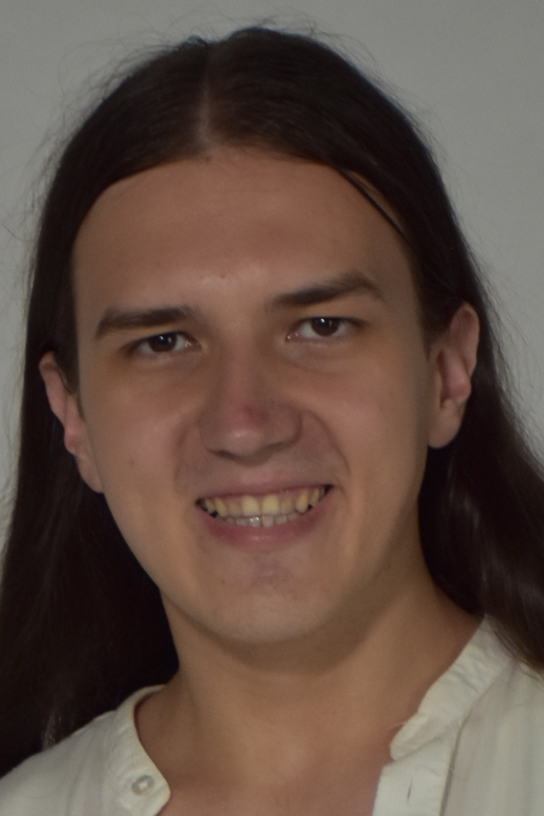 Portrait of a person with long dark hair, smiling softly at the camera, wearing a light-colored button-up shirt