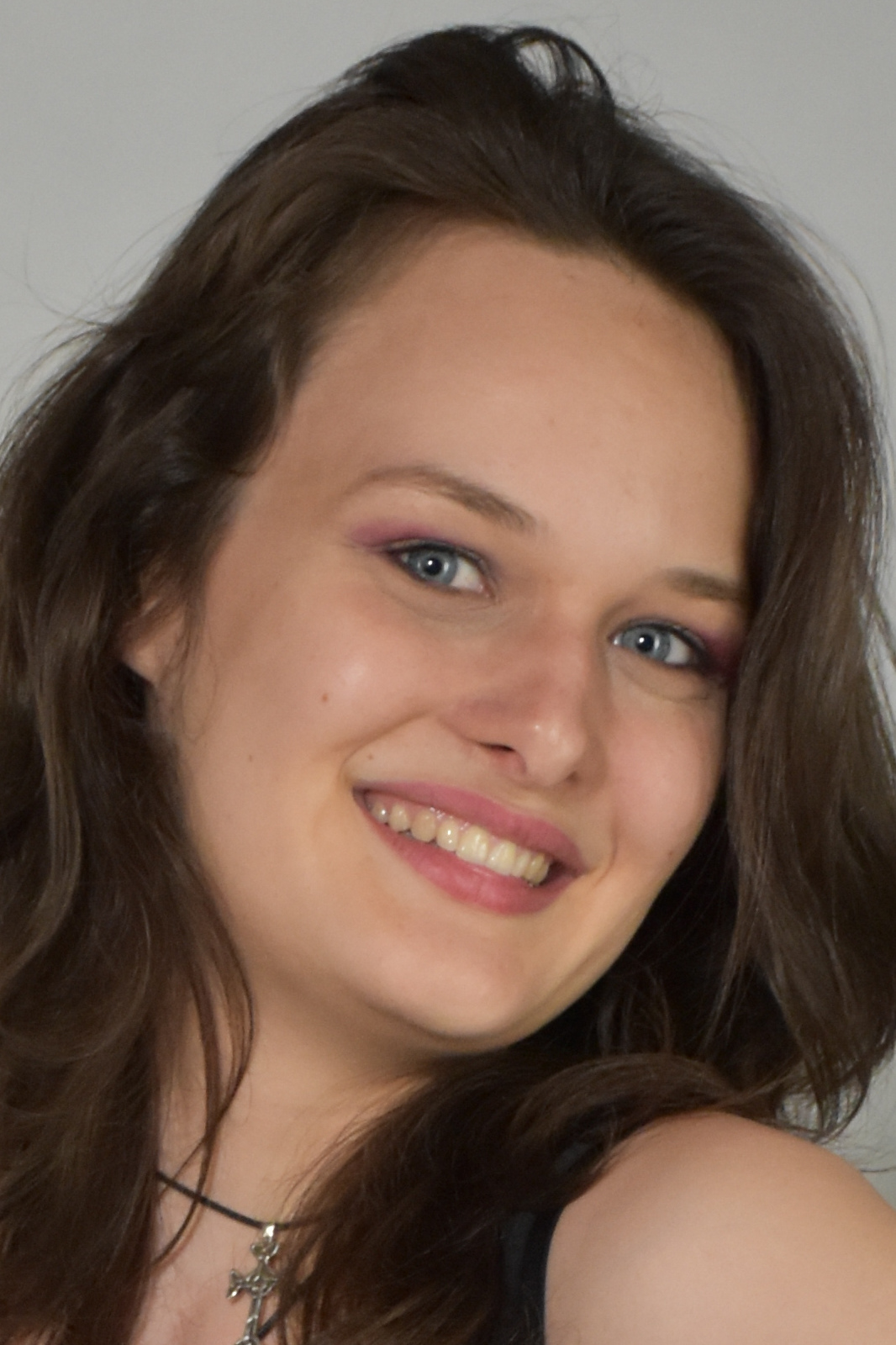 Close-up of a smiling woman with long brown hair and blue eyes, wearing a black top and a necklace.