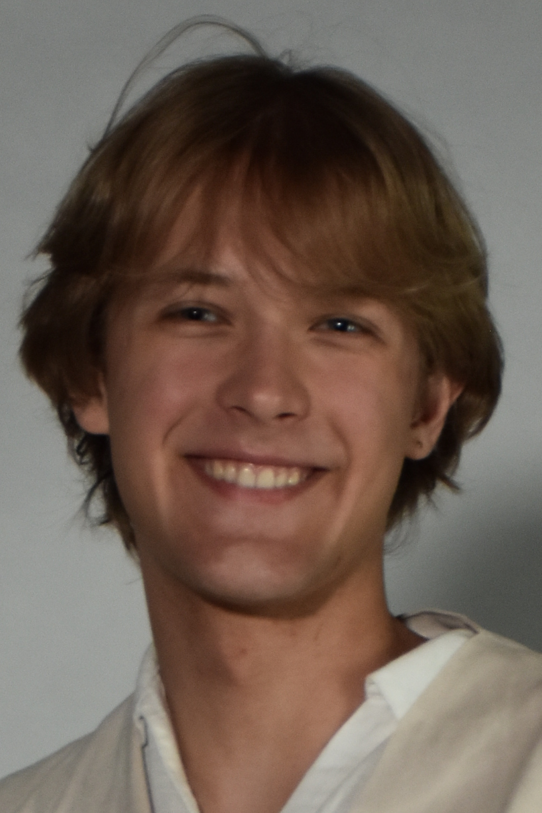 Smiling young man with light brown hair in a white shirt, facing the camera (portrait).