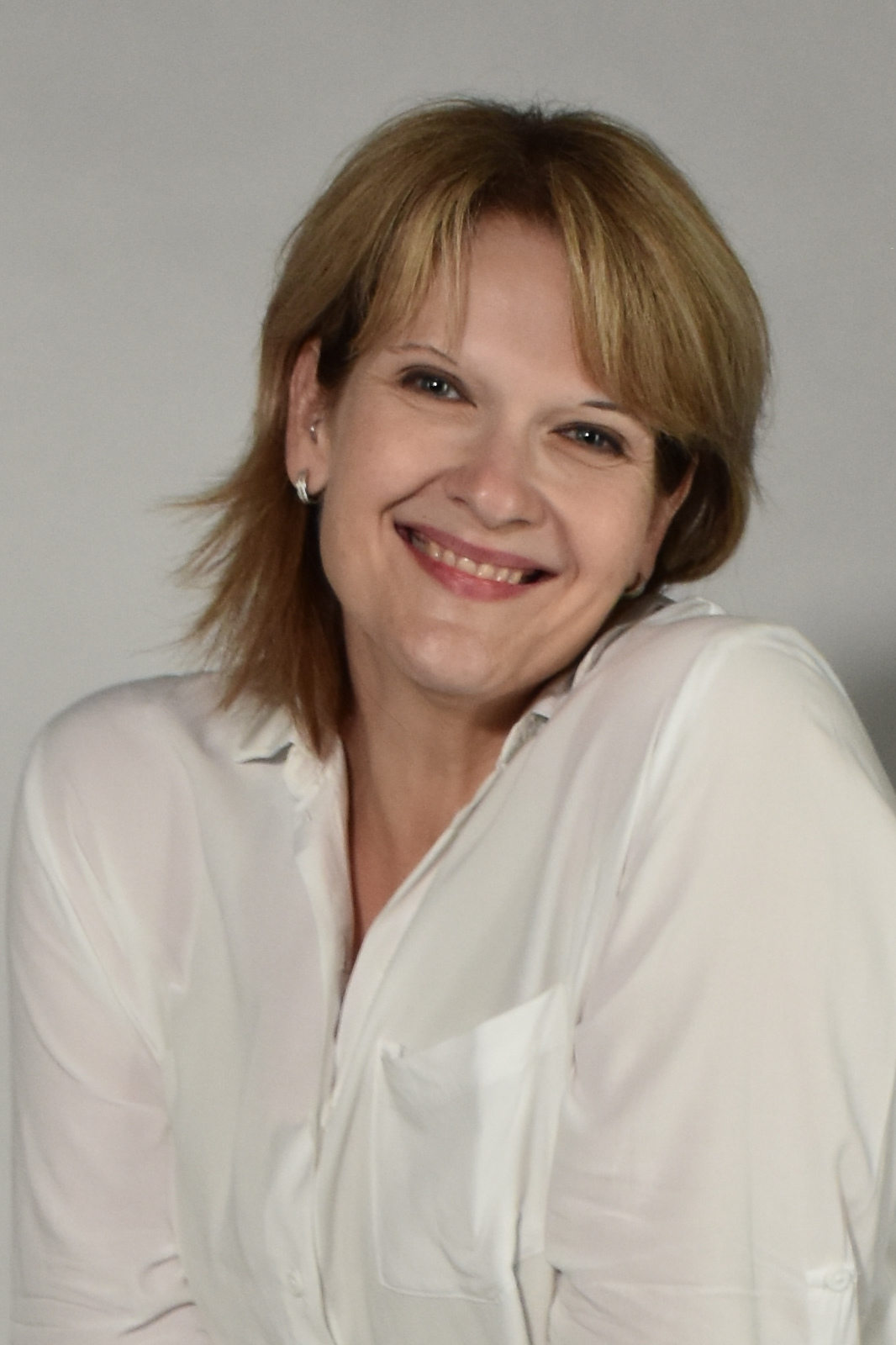Smiling woman with short blond hair wearing a white button-down shirt (head and shoulders) looking at the camera.